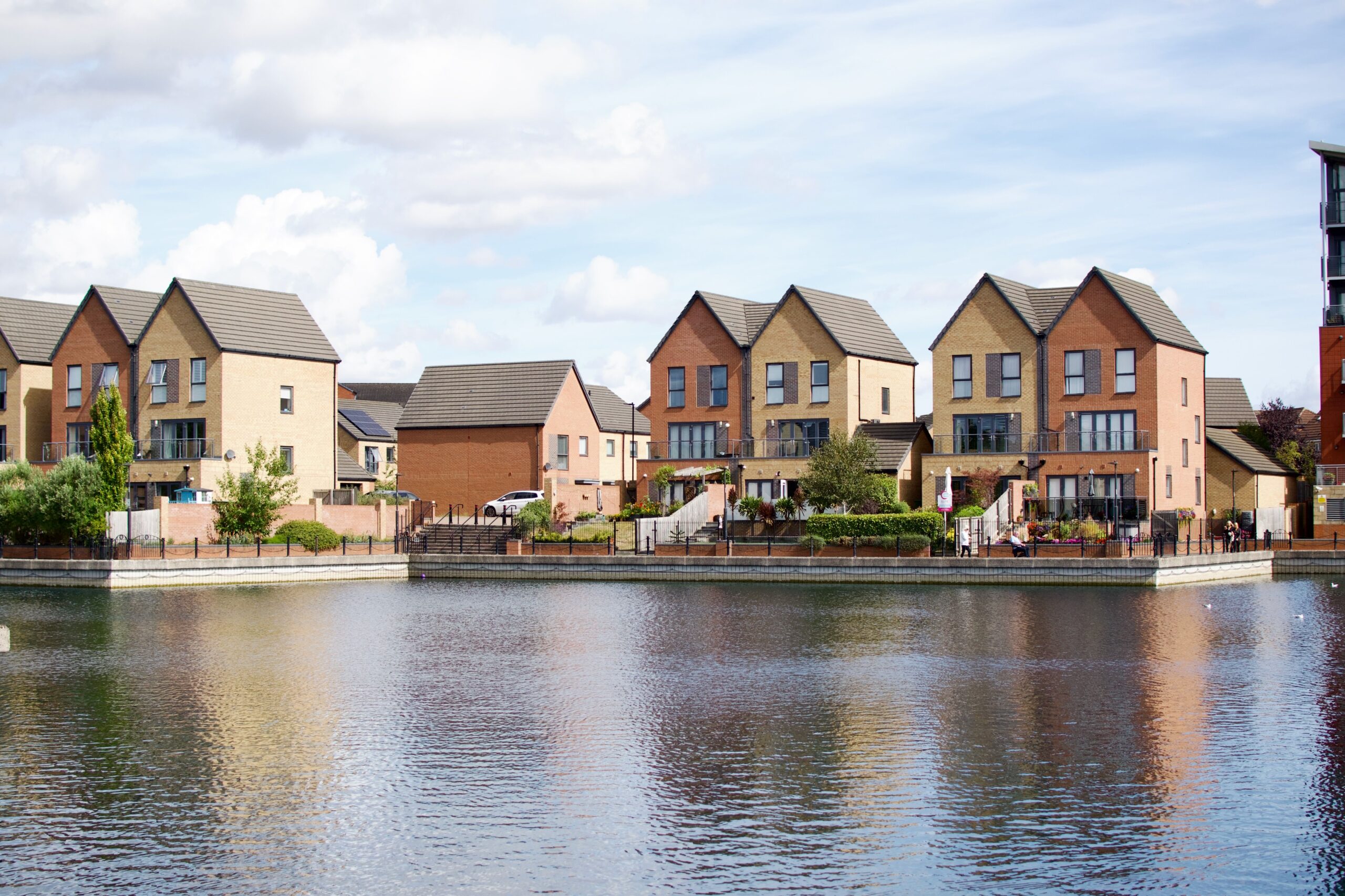 Row of modern houses by a lake with clear reflections and blue sky.